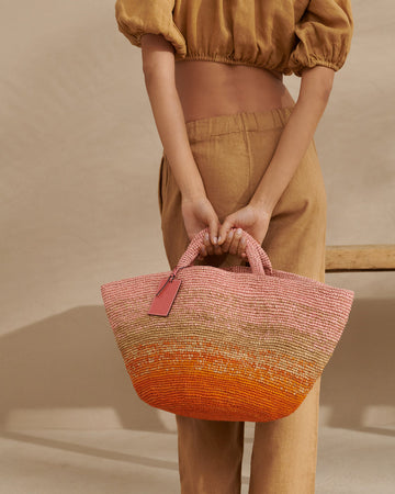 The perfect holiday bag!  Handwoven in Madagascar from durable raffia and featuring a removable soft leather tag and a slip pocket inside for your essentials and in the prettiest pink & orange combination this bag will elevate any outfit!  Perfect for strolling about on holiday!