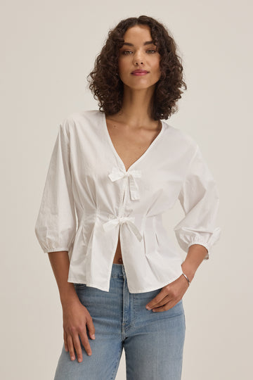 The Riri White Blouse from Velvet by Graham &amp; Spencer is crafted from their signature crisp poplin and will definitely elevate your white shirt collection!&nbsp; Featuring a flattering v neck, gathered 3/4 length sleeves and 2 self tie bows at the centre this is just perfect with your favourite denim.