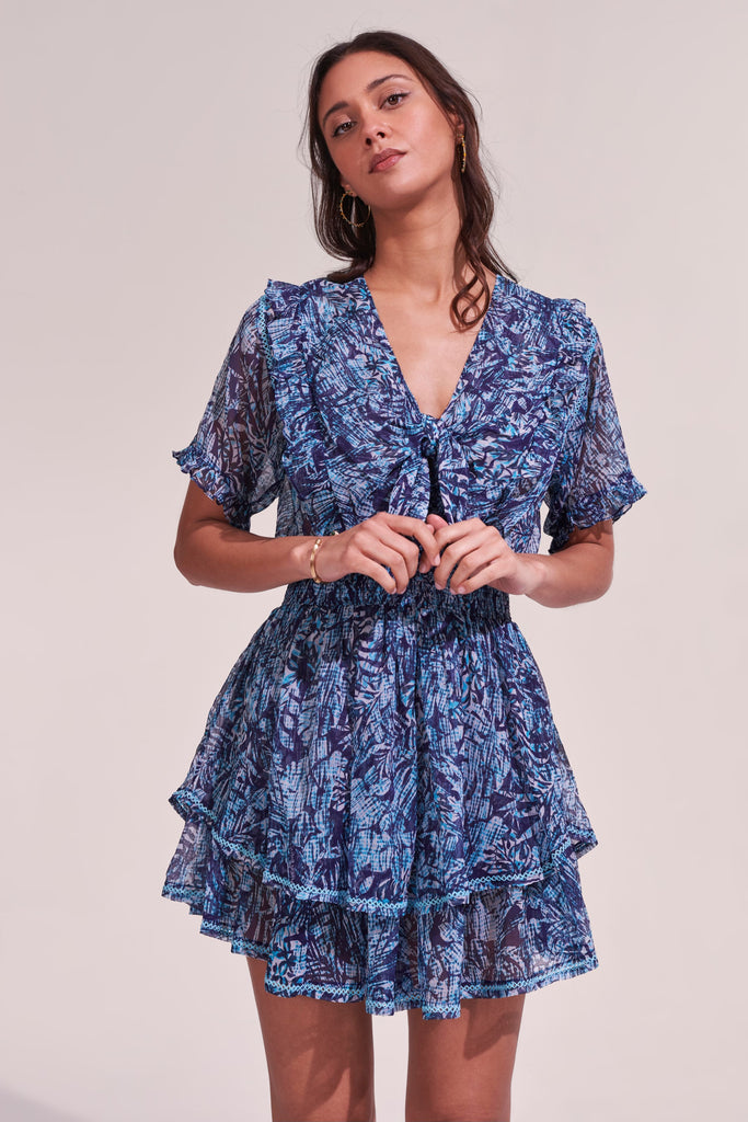 The Alyson silk crinkle mini dress from Poupette St Barth features a v-neck which ties into a bow and short sleeves with ruffle details. The elasticated waistband highlights the silhouette and leads into a tiered flared skirt.